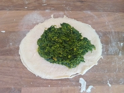 Runder Teigfladen auf einer Arbeitsfläche, welch mit Pesto bestrichen ist