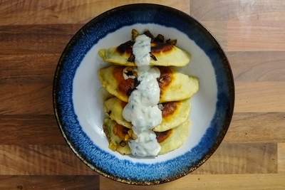 Foto von oben eines Tellers mit gebratenen Bolani, gedünstete Zwiebel und einer Knoblauchtunke
