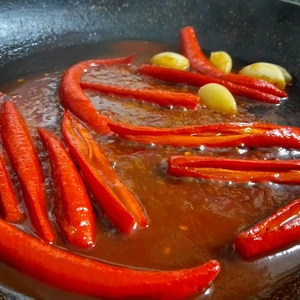 Chilis mit Knoblauch, welche in einer Flüssigkeit aus Tomatenmark, Honigersatz und Essig in einer Pfanne dünsten