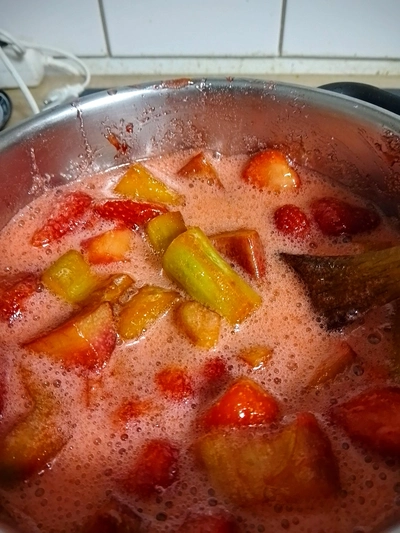Nahaufnahme des Topfes mit Zutaten aus Erdbeeren und Rhabarber in der ein Holz Kochlöffel steckt