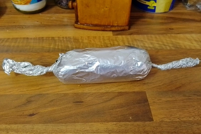 Der erwähnte Teig ist in Alufolie zu einer Wurst gerollt worden, bei dem die Enden der Alufolie zusammen gezwirbelt sind